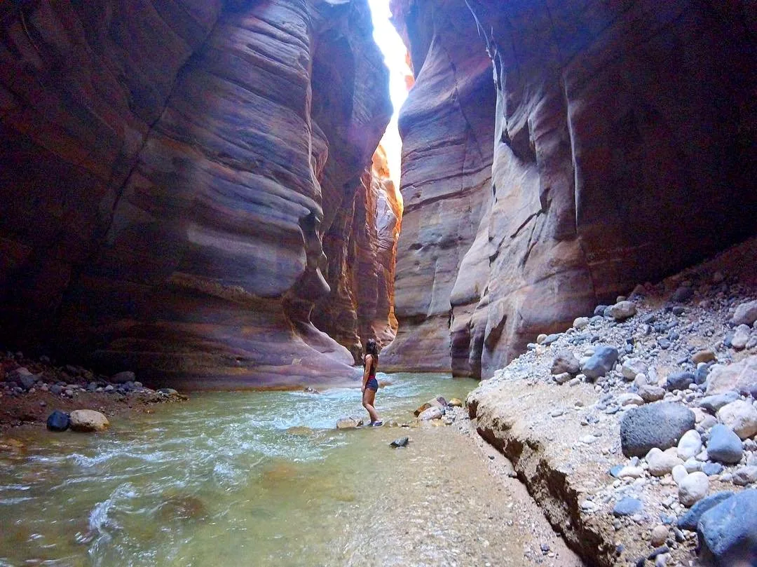 Hiker wading through water in a narrow canyon on the Wadi Mujib Siq Trail