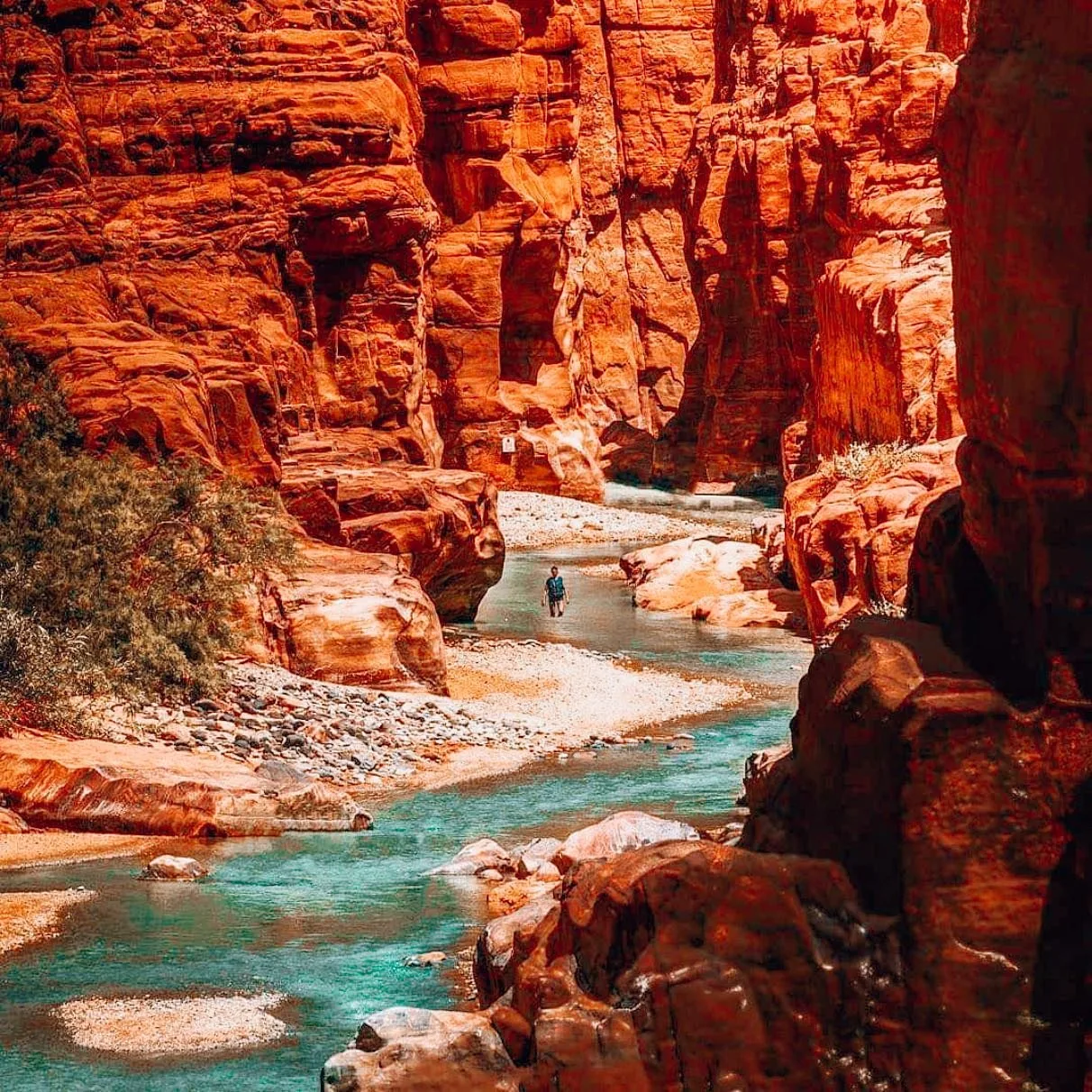 Clear turquoise water beneath red rock walls in Wadi Mujib canyon